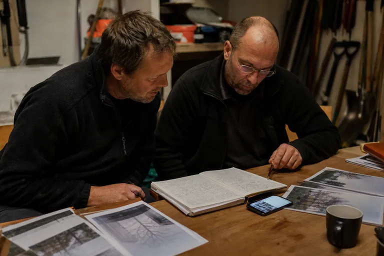 Handschriftliche Winterdienstkladde, Smartphone und ausgedruckte Fotos liegen nebeneinander auf einem Tisch.